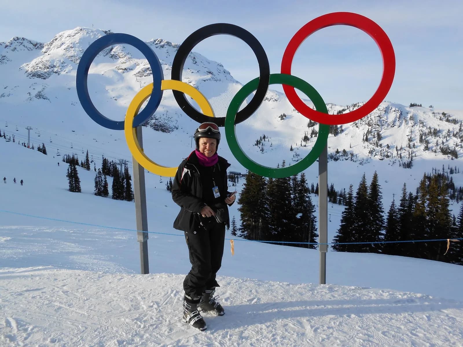Cecilia ao lado dos Anéis Olímpicos no topo de Whistler Blackcomb, com montanhas nevadas ao fundo